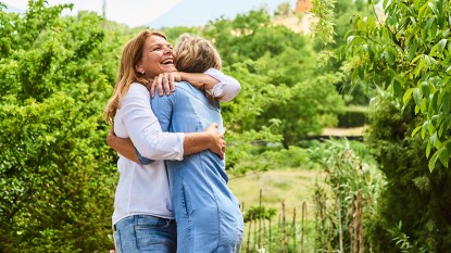 Two middle-aged women hugging outdoors