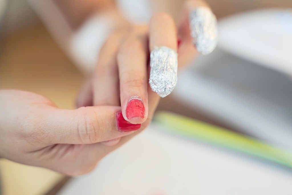 Removing gel polish nails from fingernails with a cotton ball soaked in acetone then wrapping nails with aluminum foil