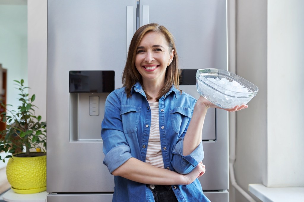 Woman holding ice cubes in front of fridge with ice maker