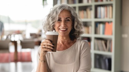 A woman with grey hair in tan top holding a cup of coffee to ward off diabetes