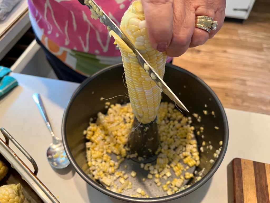 woman removing kernels from corn on the cob into a bundt pan