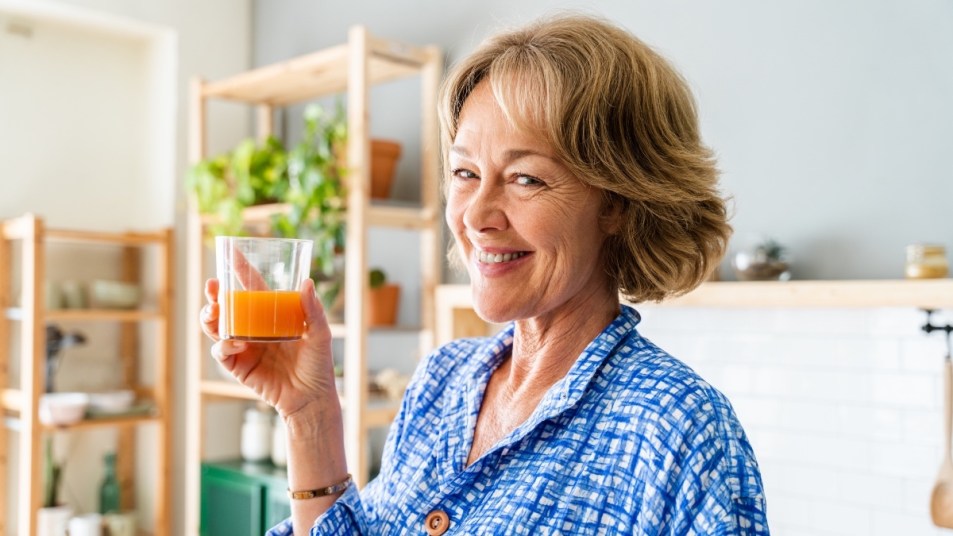 A woman with short hair in a blue shirt holding an orange juice adrenal cocktail