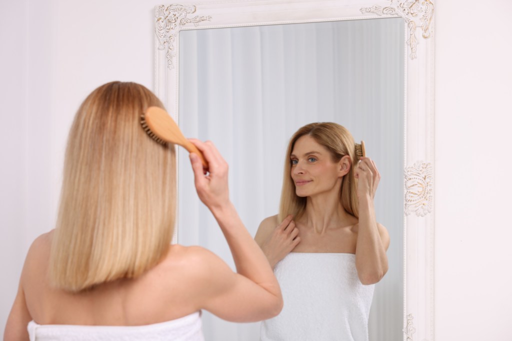 Mature woman looking in mirror while brushing hair