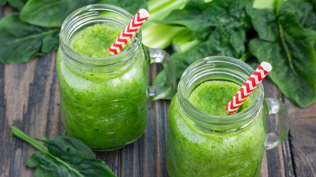 A green spinach adrenal cocktail smoothie in a clear glass with a red and white straw