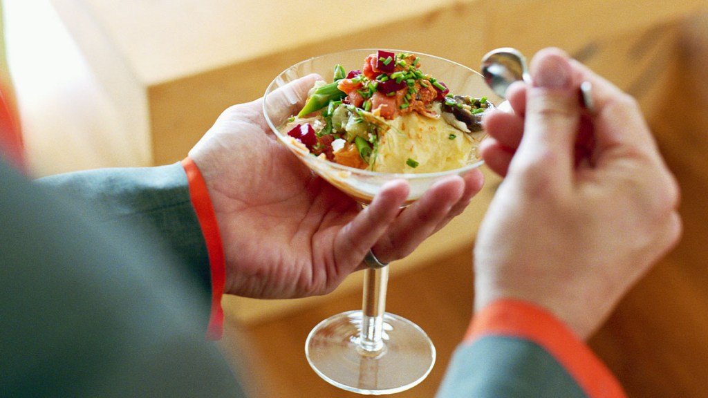 Person holding a martini glass filled with mashed potatoes topped with bacon and scallions, at a mashed potato bar party