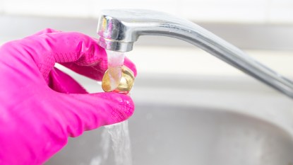 Hand wearing a pink glove cleaning a gold ring at home under sink