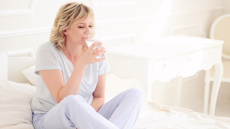 woman in bed drinking water after waking up with dry mouth