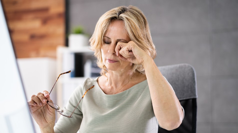 Dry eye: Woman at a computer rubbing her eyes