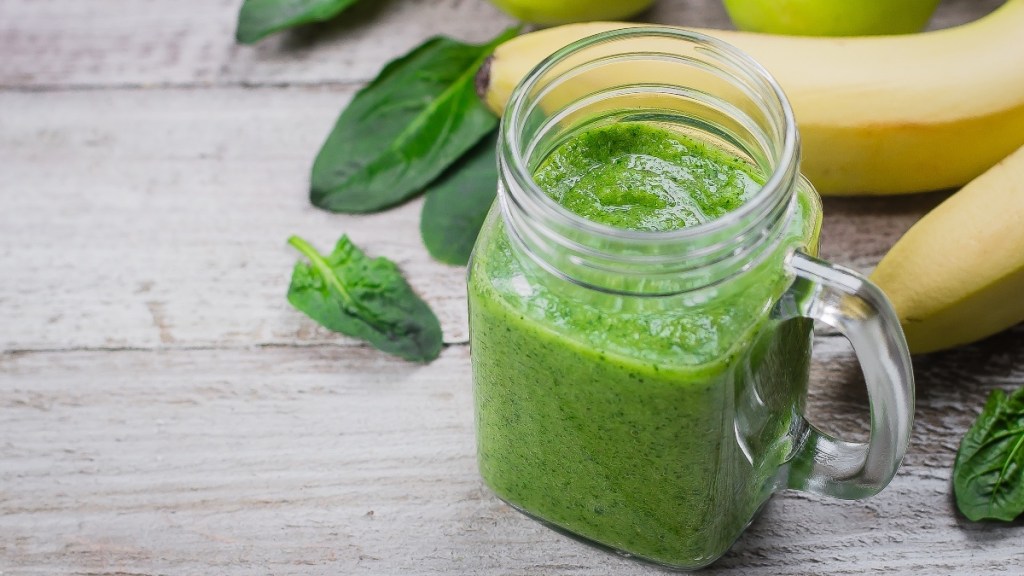A Mason jar with a green smoothie and bananas in the background, with is packed with dietary fiber for mood