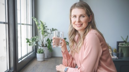 A woman in a pink shirt holding a glass of water to take quercetin and zinc for their health benefits