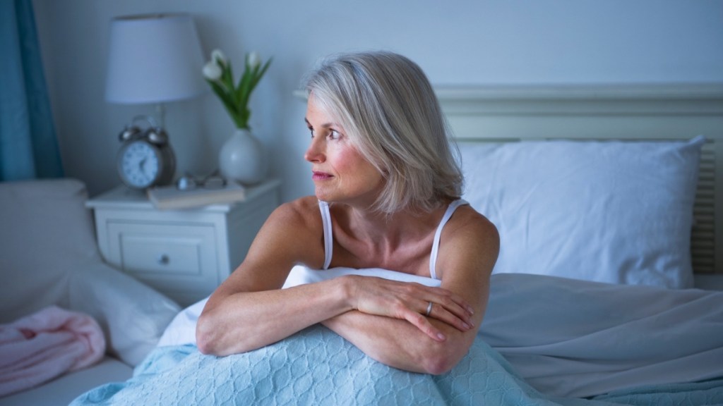 A woman sitting up in bed who can't sleep and uses supplements to reduce cortisol