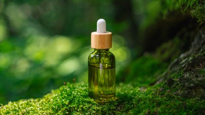 A vial of tea tree oil sitting on moss about to be used to treat eczema