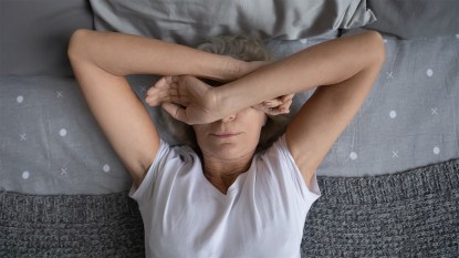 tired woman laying in bed: alpha gal syndrome symptoms