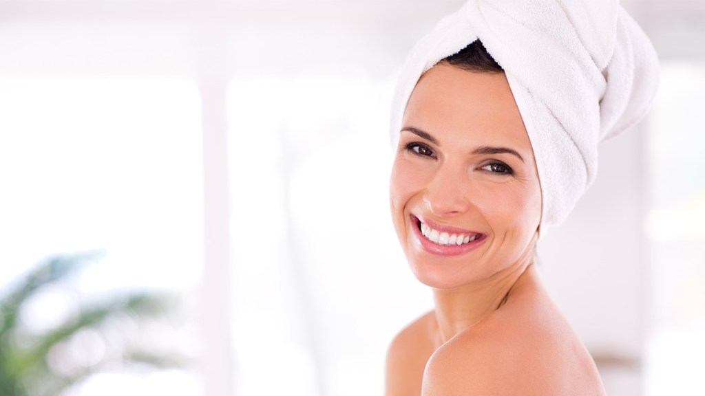Woman smiling wearing a towel and with her hair wrapped in a towel after taking an everything shower