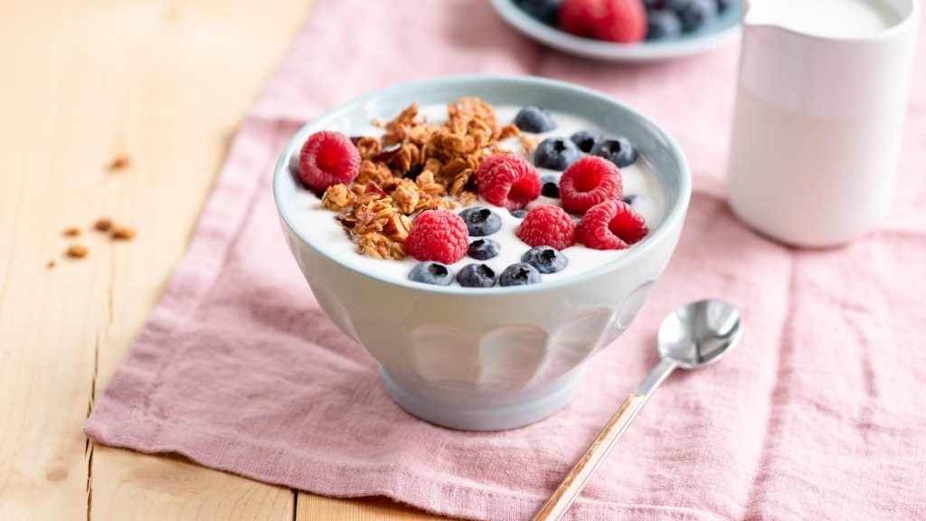 A bowl of yogurt, blueberries, raspberries and granola on a pink napkin on a table