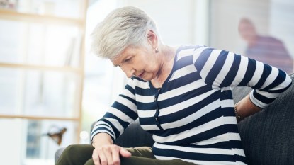 A grey haired woman in a striped shirt holding her mid back, which is in pain