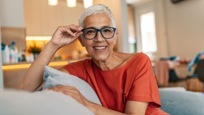 A woman with grey hair and an orange shirt wearing glasses who has macular degeneration