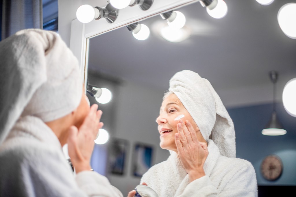 Mature woman applying moisturizer in mirror
