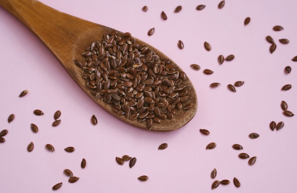 Flax seeds on wooden spoon and pink background