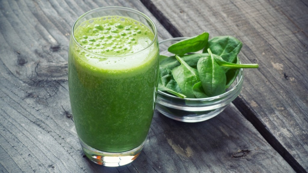 A glass of a green smoothie beside a bowl of spinach that can help reduce the risk of macular degeneration