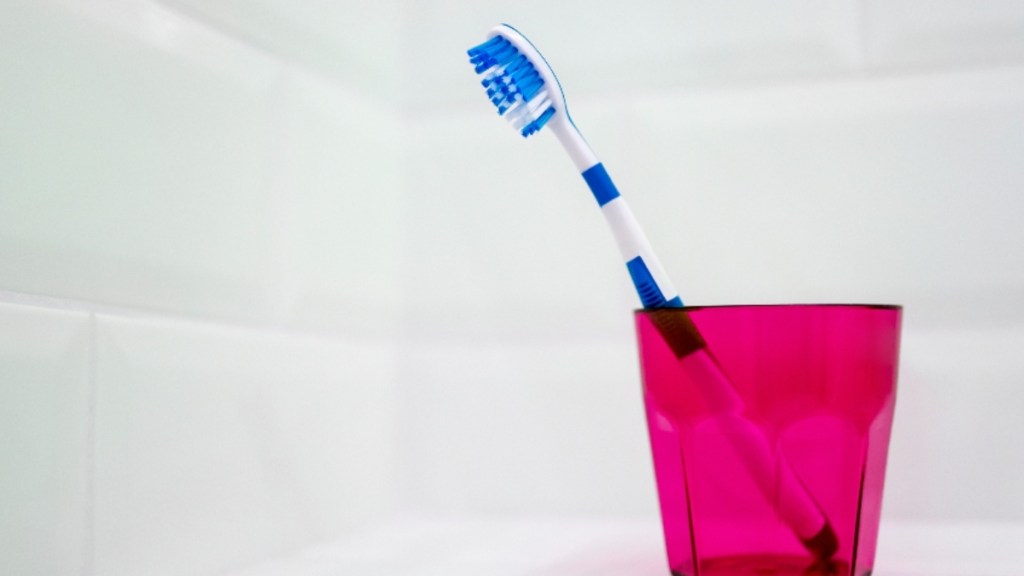 A still life of a single blue toothbrush standing alone in a pink toothbrush holder in a white tiled bathroom (How to clean a toothbrush)