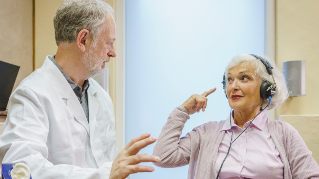 A senior woman wearing headphones getting a hearing test with an older male doctor in a white lab coat