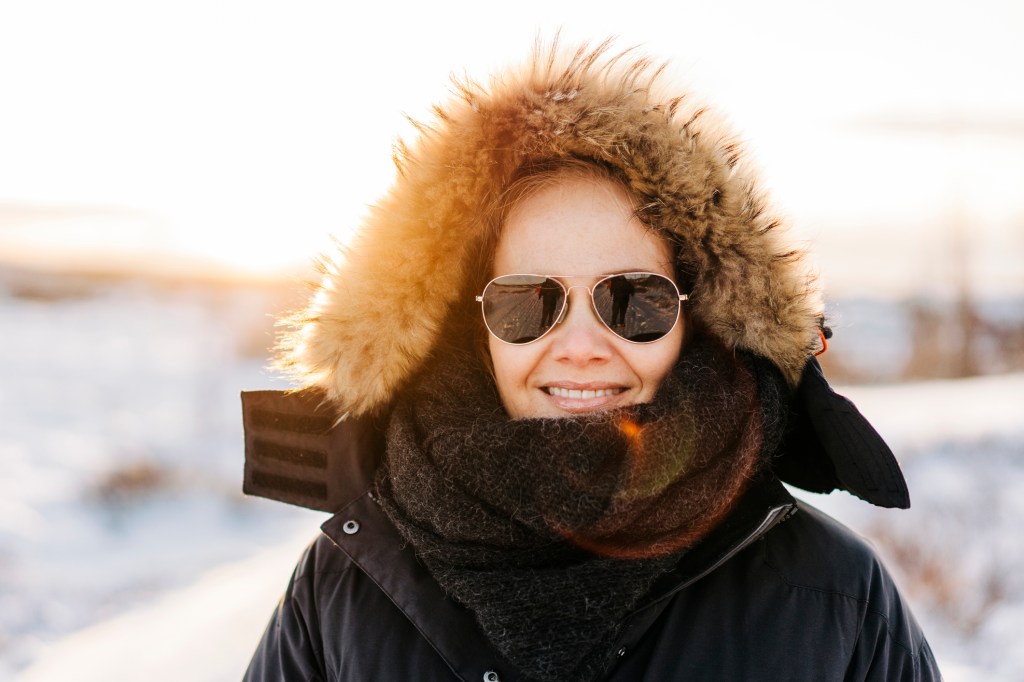 Mature woman outside in winter with sun shining and sunglasses on with fur hood up