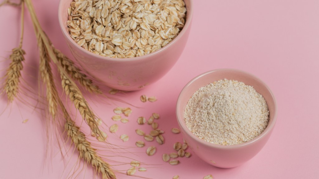 A bowl of whole oats, a bowl of colloidal oats and fresh wheat on a pink background