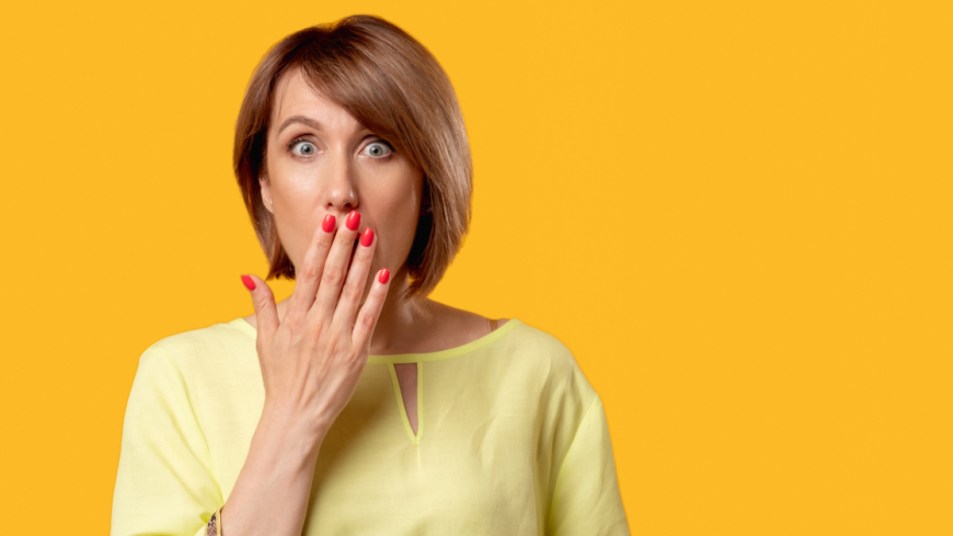 A woman with short hair and red nails covering her hand with her mouth to eliminate bad breath from the stomach