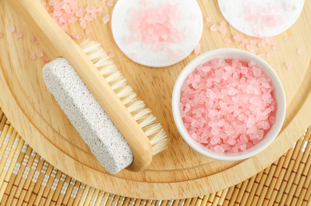 Bowl of pink Himalayan bath salt next to foot scrubber