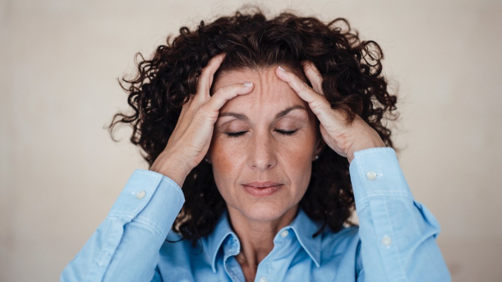 A woman holding her hands to her head with her eyes closed due to stress