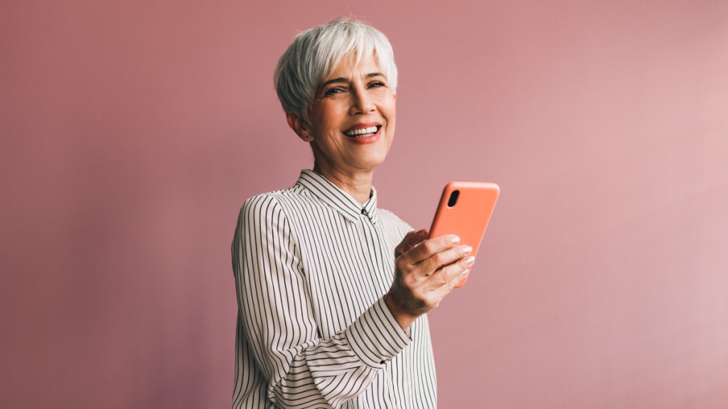 A woman with short grey hair wearing a striped shirt holding a cell phone