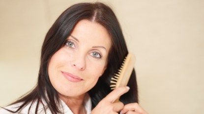 A woman with dark hair who has a vitamin deficiency that causes hair loss brushing her hair with a wooden brush