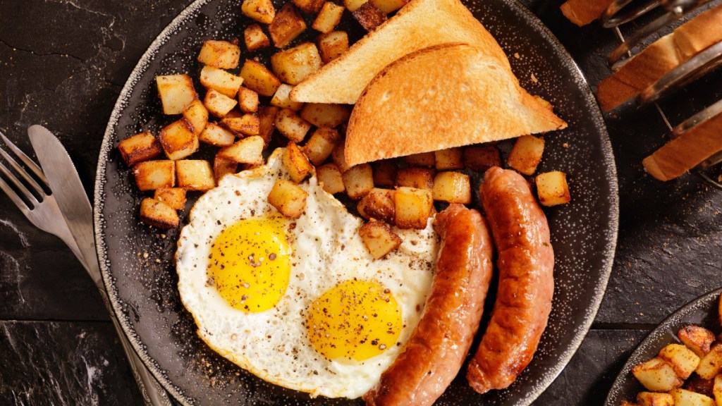 A breakfast plate of two eggs, two sausages, slices of bread and diced potatoes