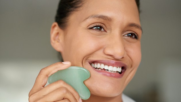 Woman smiling and using a gua sha tool