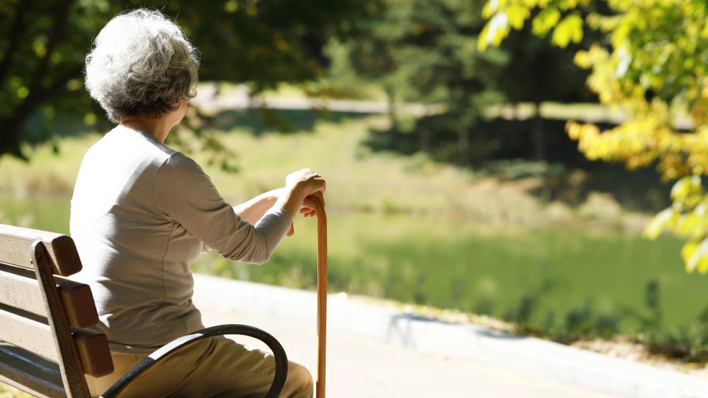 An elderly woman holding a cane while sitting on a park bench