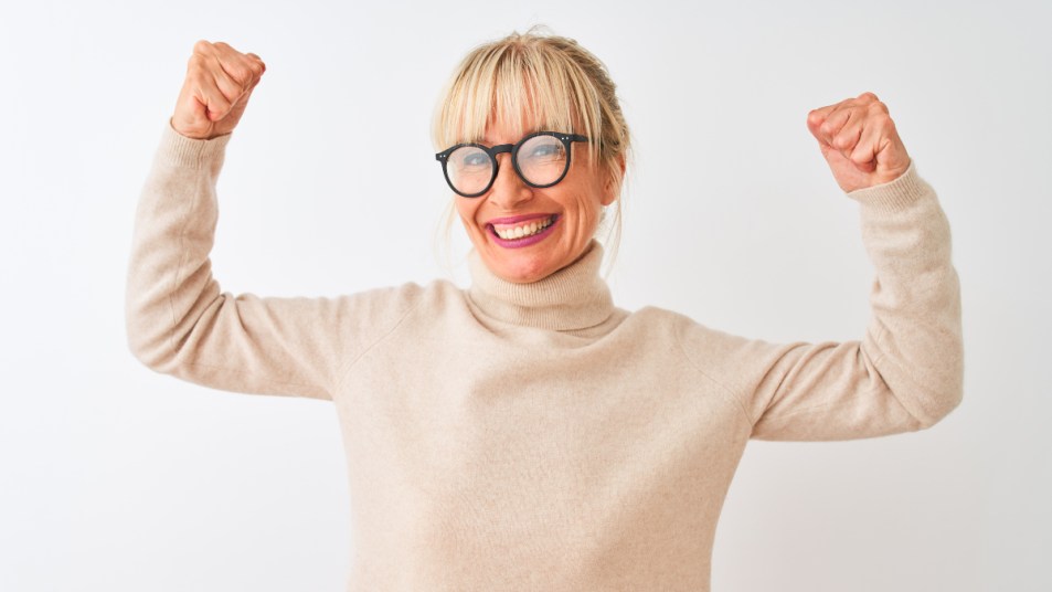 A woman in a turtleneck and glasses flexing her arms thanks to taking the vitamin that stops age-related muscle loss
