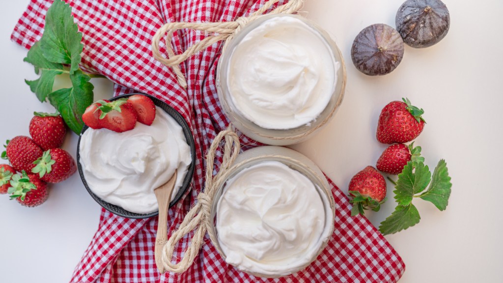 Bowls of yogurt, which contain probiotics that help with bloating, next to fresh fruit and a red and white checkered napkin