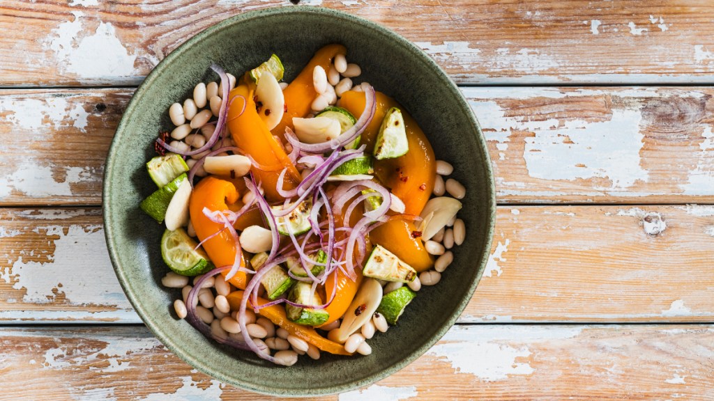 A white bean salad with vegetables in a bowl on a rustic wooden table