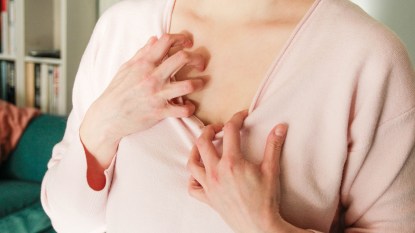 A close-up of a woman in a pink shirt scratching her chest due to breast eczema