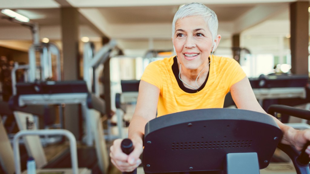 A woman with grey hair and a yellow shirt using an exercise bike at a gym
