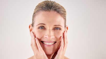 Woman touching her face and smiling. Her complexion looks healthy after doing skin barrier repair treatments