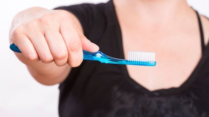 woman holding toothbrush after getting toothpaste on her shirt