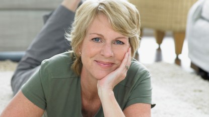 Happy woman lying on stomach on floor with chin in hand