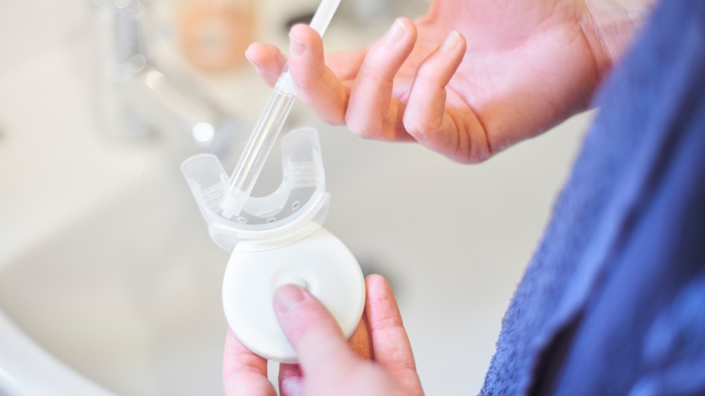 A close-up of a hand applying a whitening gel to a home tooth whitening device