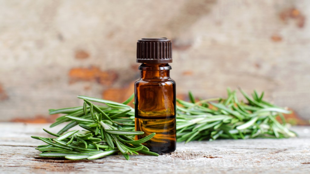 An amber essential oil vial next to fresh rosemary, which 