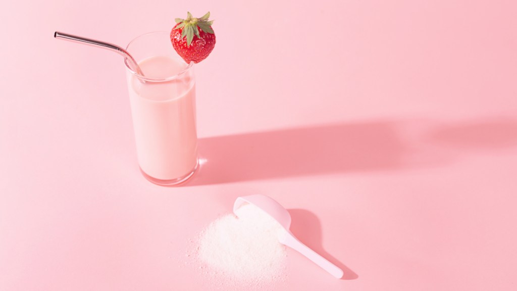 A pink berry smoothie on a pink background beside a scoop of protein powder, which helps reverse hair loss caused by Ozempic