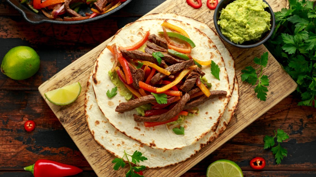 Steak fajitas on tortillas topped with bell peppers and a dish of guacmole