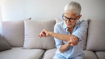 A woman with grey hair wearing a striped shirt holding her elbow, which is in pain due to early warning signs of psoriatic arthritis