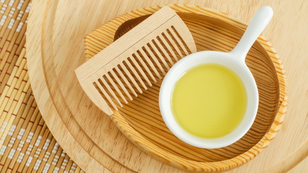 A bowl of castor oil beside a brush set on a wooden tray to help combat hair loss caused by Ozempic